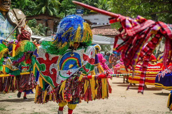 Grupo de pessoas celebrando o Maracatu, com trajes coloridos e instrumentos.